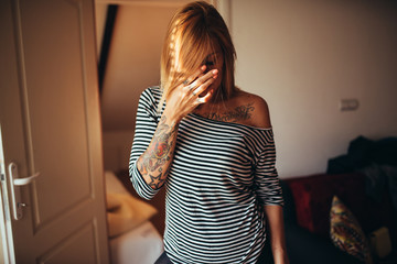 Young tattooed woman standing at home