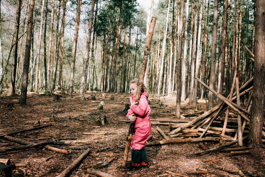 young blonde girl carrying a large log in the middle of a forest
