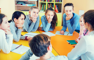 Friendly female teacher talking to children, sitting together around desk