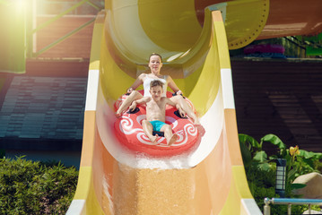 European boy and mother slides down water slider on floater at waterpark. - 280271847