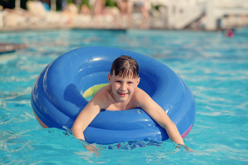Portrait of European boy swimming in rubber ring in pool on summer vacation.
