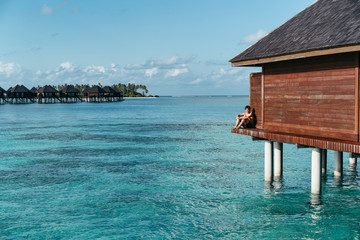 A man seated in a water villa in Maldives islands enjoying the turquoise water.