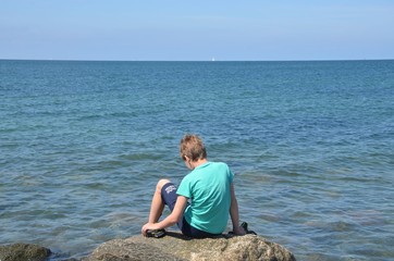 Kind sitzt auf einem Stein am Meer - Ostsee