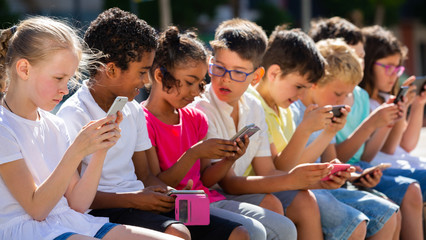 Smiling children sitting at urban street with mobile devices