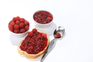 Red raspberries in a cup and toast with jam and fresh raspberries on a white isolated background, selective focus, copy space .
