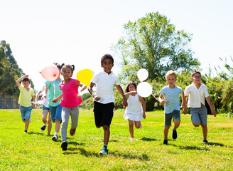 Cheerful kids with balloons are jogging together in the park and having fun