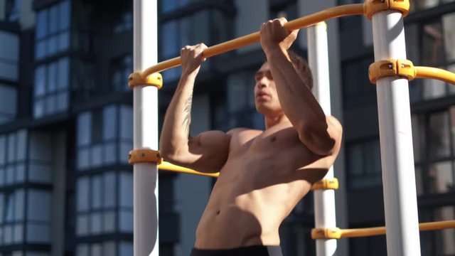 Muscular man doing pull-ups on horizontal bar. on workout area near house