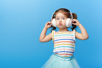 Happy smiling child enjoys listens to music in headphones over colorful bleu background. Vivid and fun emotions, happy child with pleasure listens to songs in wireless headphones