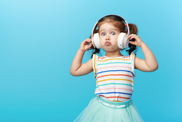 Happy smiling child enjoys listens to music in headphones over colorful bleu background. Vivid and fun emotions, happy child with pleasure listens to songs in wireless headphones
