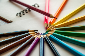 Fototapeta premium Fifteen multi-colored pencils are lying around and one on top on white sheets of paper