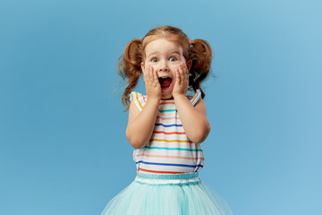 Portrait of surprised cute little toddler girl child standing isolated over blue background....