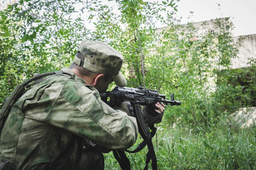 military crouching aims from a Kalashnikov in the woods