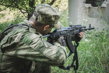 military crouching aims from a Kalashnikov in the woods