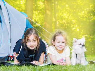 Camp in the tent - girls with little dog chihuahua sitting together near the tent. Camping with children. Camping tourism and vacation concept