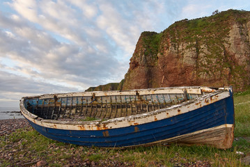 An Old Wooden Scottish Fishing Boat, long abandoned, lies on the Pebble Beach by the Fishing...