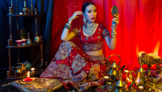 Beautiful young indian woman in traditional Sari clothing with Oriental Jewelry looking in the mirror and trying on jewelry
