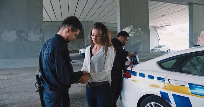 Police in action. View of two policemen detaining and arresting dangerous drug dealer young woman in the street. Protection and security concept.