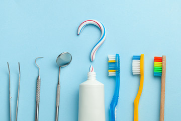 Question mark from toothpaste. Tube of colored toothpaste and  toothbrush and dentist tools, mirror, hook on blue background. The concept of choosing good toothpaste for brushing your teeth