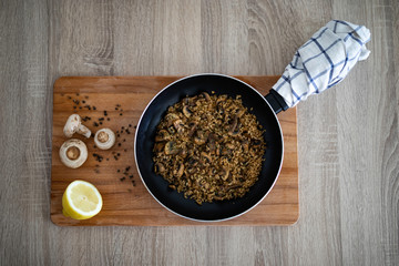 Pan with mushrooms risotto on a wooden cutting board decorated with garlic, pepper, lemon and mushrooms