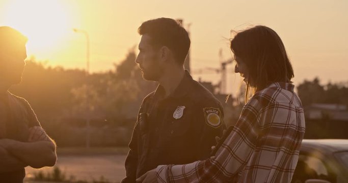 Professional policeman at work questions two drivers man and woman arguing and charging each other about the car accident at sunset in the city.
