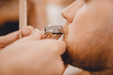 Close-up of barber shaving beard to man in barbershop