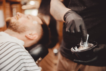 Brush for shaving beard along with bowl, blurred background of hair salon for men, barber shop