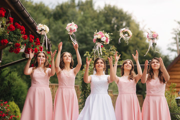 Happy bride with bridesmaid hold bouquets and have fun outside. Beautiful bridesmaid in same...