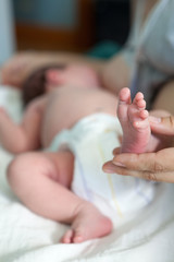 Newborn infant barefoot leg in women hand, mother breastfeeding baby lying in bed, close up view