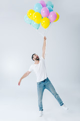 excited man in casual clothes holding colorful balloons on grey