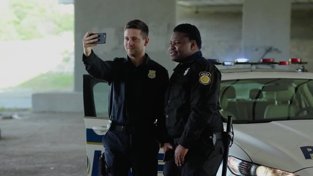 Portrait funny two men cops stand near patrol car take selfie smile accepting emergence call enforcement talk look around officer police uniform auto safety security colleagues policeman slow motion