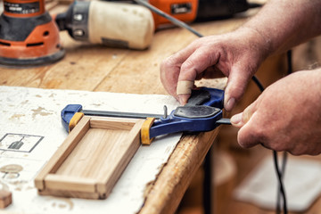 Close-up senior carpenter glueing wooden craft surface and joining with clamps. Woodwork carpenter...