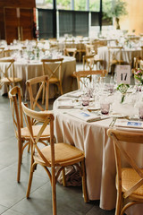 Tables and wooden chairs arranged and decorated in a wedding hall of a hotel