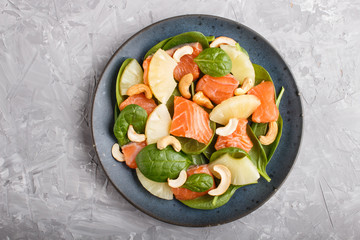 Fresh salmon with pineapple, spinach and cashew in blue ceramic plate on a gray concrete background.
