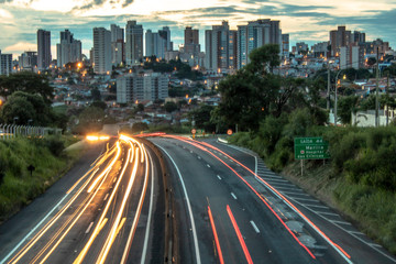 Obraz na płótnie Canvas Trail of light caused by vehicular traffic in SP-294, Comandante Joao Ribeiro Barros Highway with buildings from downtown in the background, in Marília, during a late afternoon.