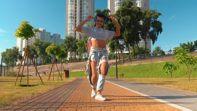 happy mixed race teenager walking and dancing on the street girl wearing jeans and casual shirt listening music on the run