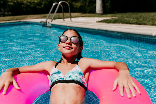 beautiful teenager girl floating on pink donuts in a pool. Wearing sunglasses and smiling. Fun and summer lifestyle