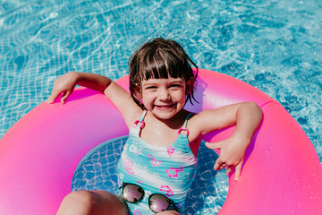 beautiful kid girl floating on pink donuts in a pool. Wearing sunglasses and smiling. Fun and summer lifestyle