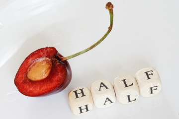 A half of red sweet cherry on a light background next to the cubes with letters. Macro and training