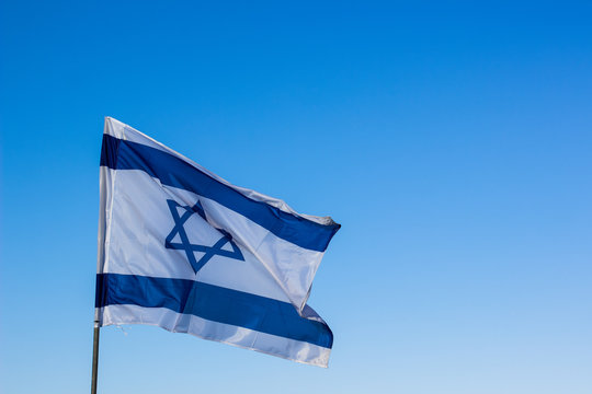 Israeli national flag evolving on a wind on empty blue sky background with copy space for text