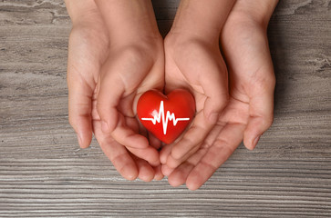 Woman and child holding heart on wooden background, top view. Donation concept