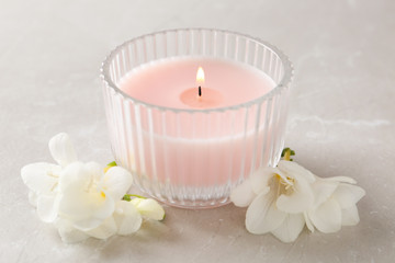 Fototapeta na wymiar Lit candle and beautiful flowers on grey marble table