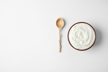 Bowl of sour cream and wooden spoon on white background, top view