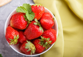 Fresh red strawberry in white bowl on gray concrete background. top view.