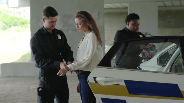 Young woman arrested by police officers and handcuffed sitting in patrol car criminal handcuffs justice policeman black broadcast robbery burglar drugs male prisoner slow motion