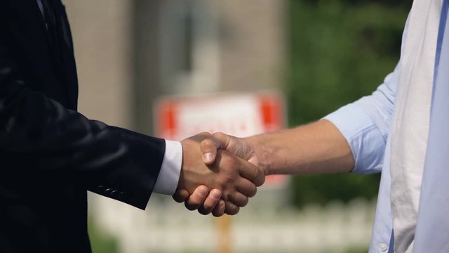Two man shaking hands on background of sold signboard, successful house buying