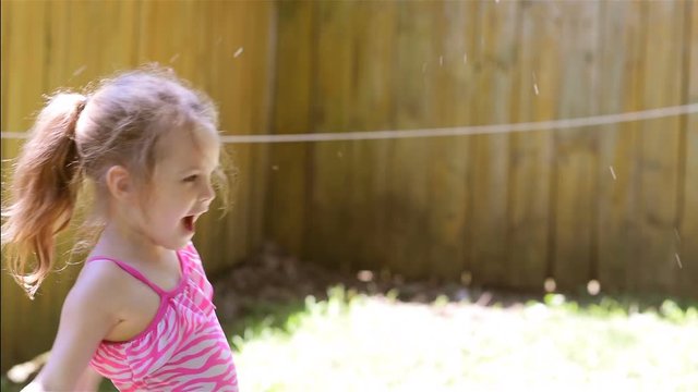 A female child plays with a back yard water hose in summer