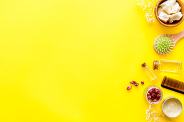 Bottle with jojoba, argan or coconut oil, styling, comb for hair style on yellow background top view mock up