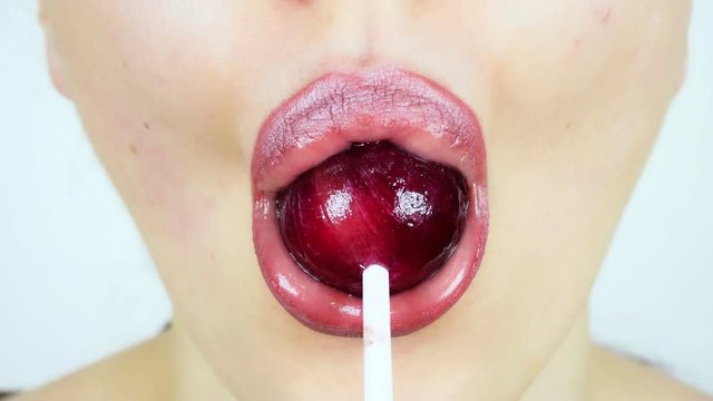 Extreme close-up of young woman's lips. A woman is licking a big lollipop. Femalebright make-up for lips