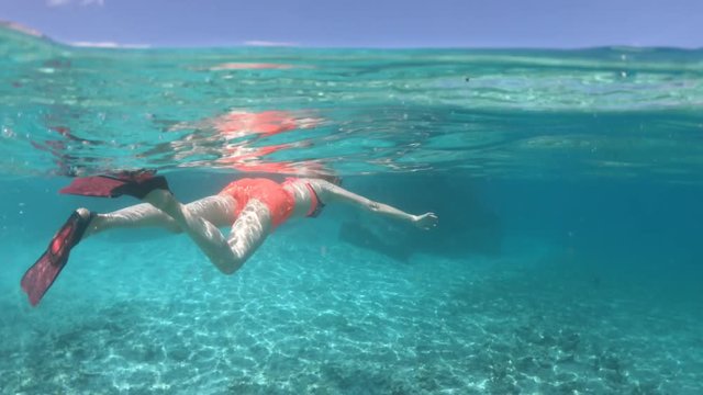Third person view of girl snorkeling underwater at St. Pierre Island. Split view of woman exploring sea life of Indian Ocean, under and above water. Coral reef landscape of Seychelles.