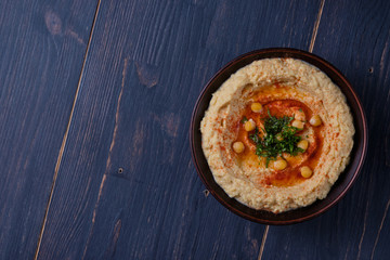Classic hummus with hot pepper in a clay plate on a wooden table. National, vegetarian dish. General form.